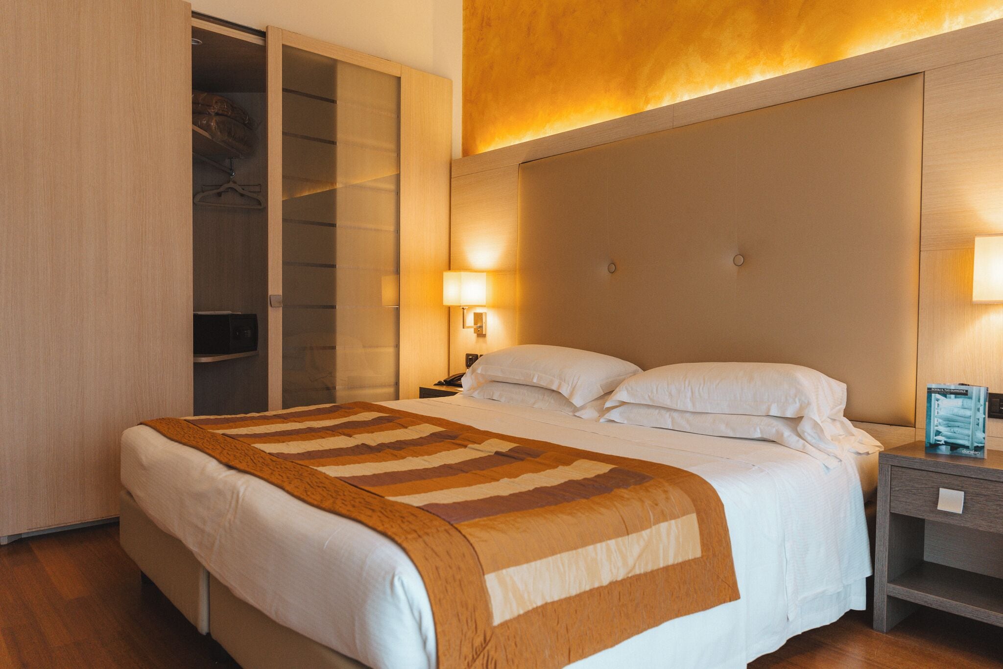 Una habitación de hotel con cama, mesita de noche, lámpara y armario.