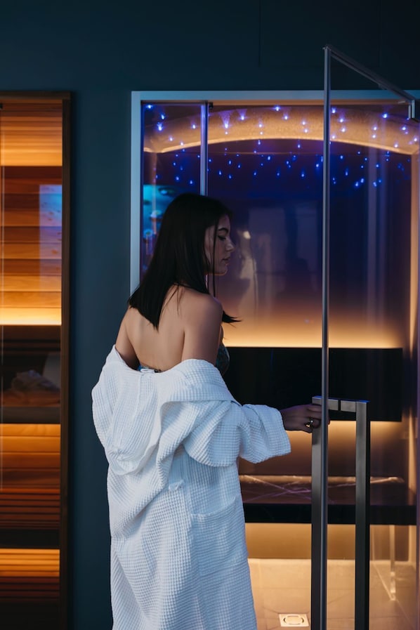 A person in a white robe standing in front of a large window with a view of a cityscape at night.