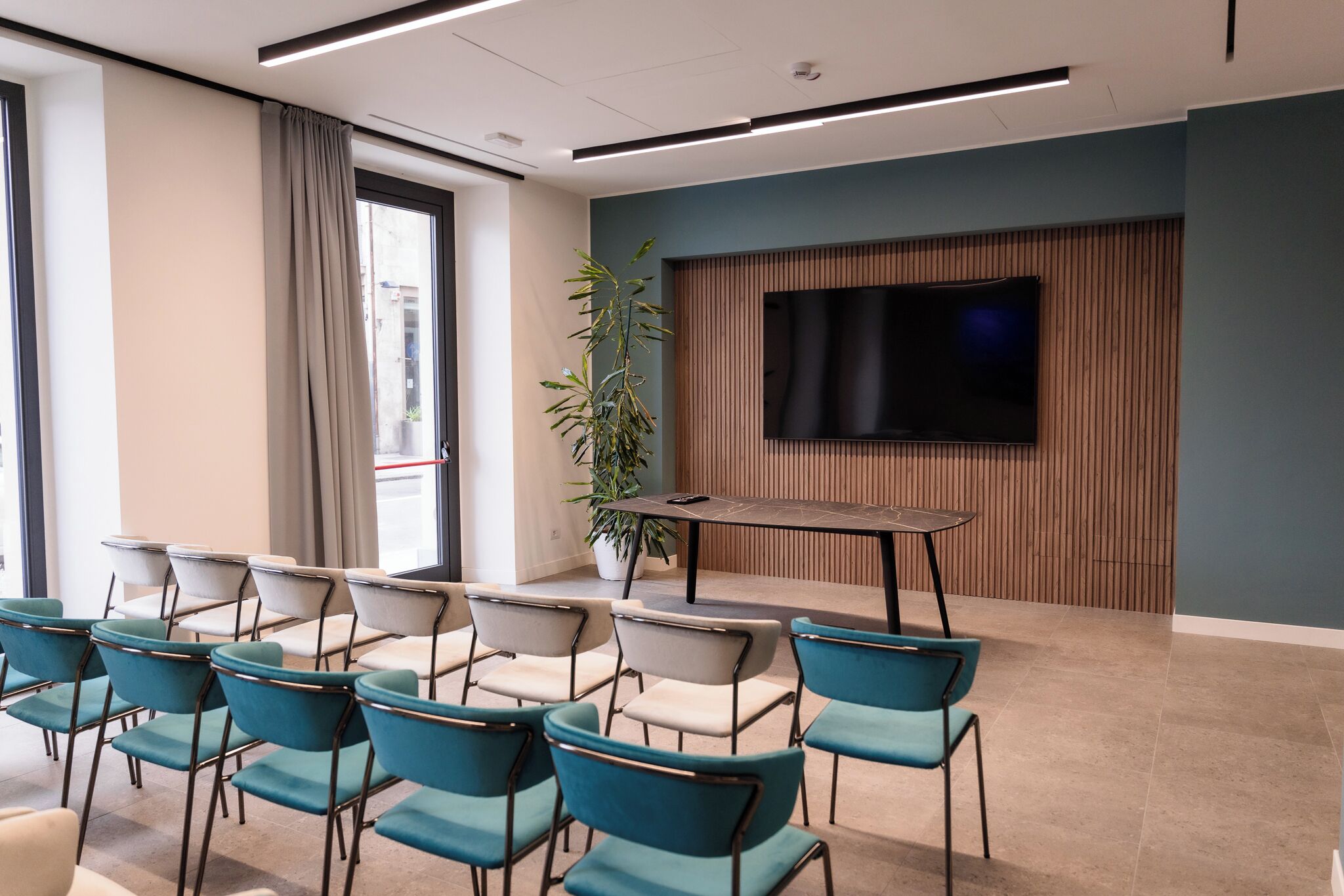 A conference room with teal chairs, a table, a large TV, and a potted plant.