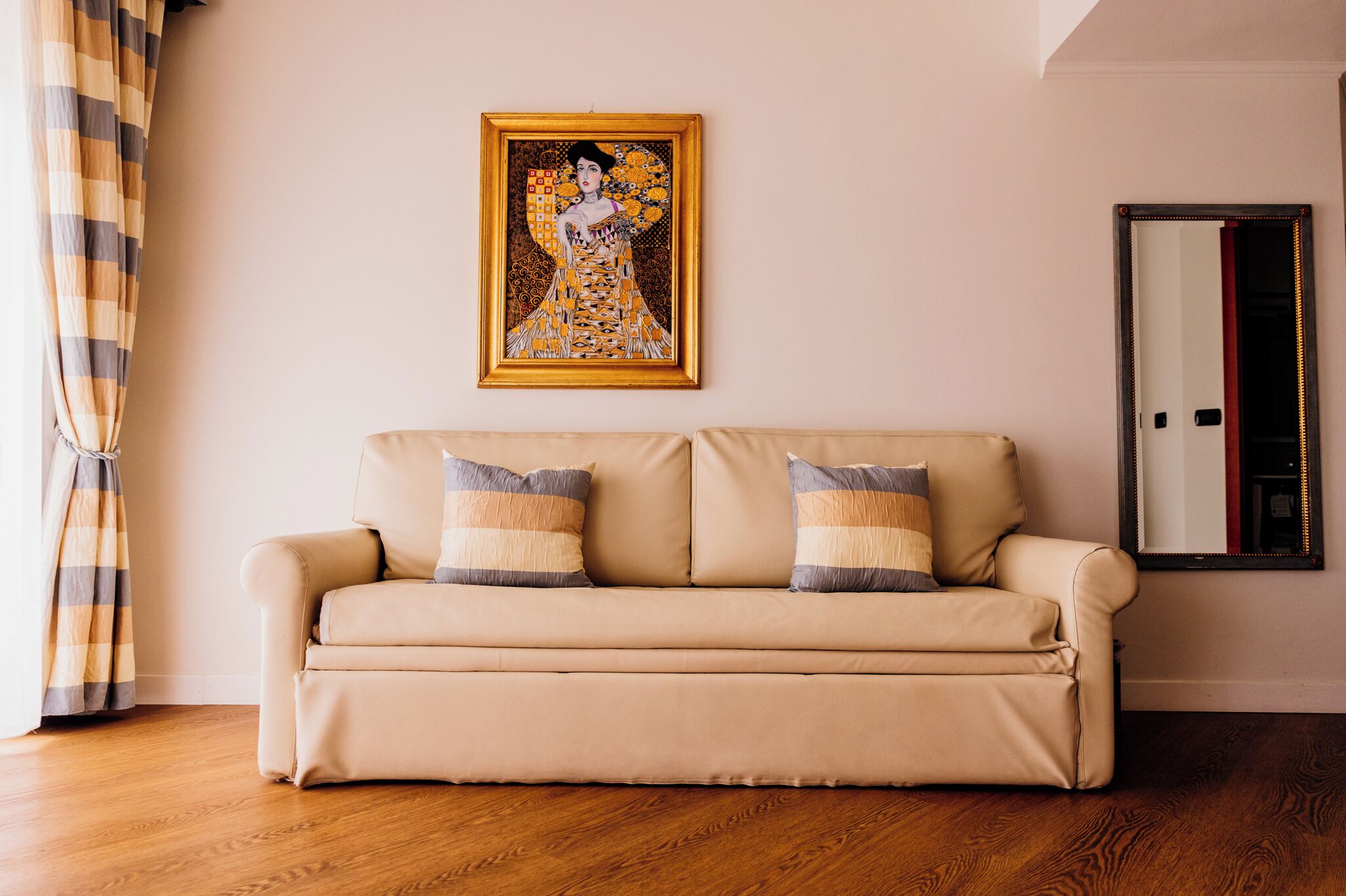 A beige sofa with striped pillows, a framed artwork above it, and a mirror on the wall.
