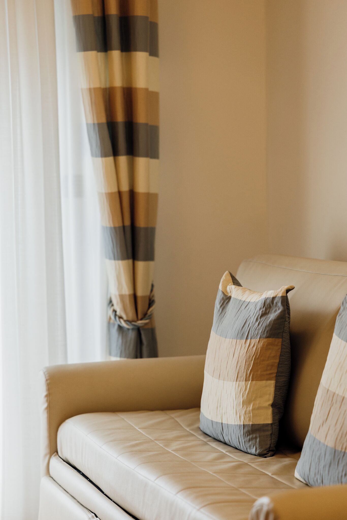 Un sofá con un cojín, una ventana con cortinas y una pared.