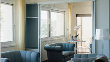 A room with a large window, a seating area with blue chairs, a table with a vase of flowers, and a mirror.