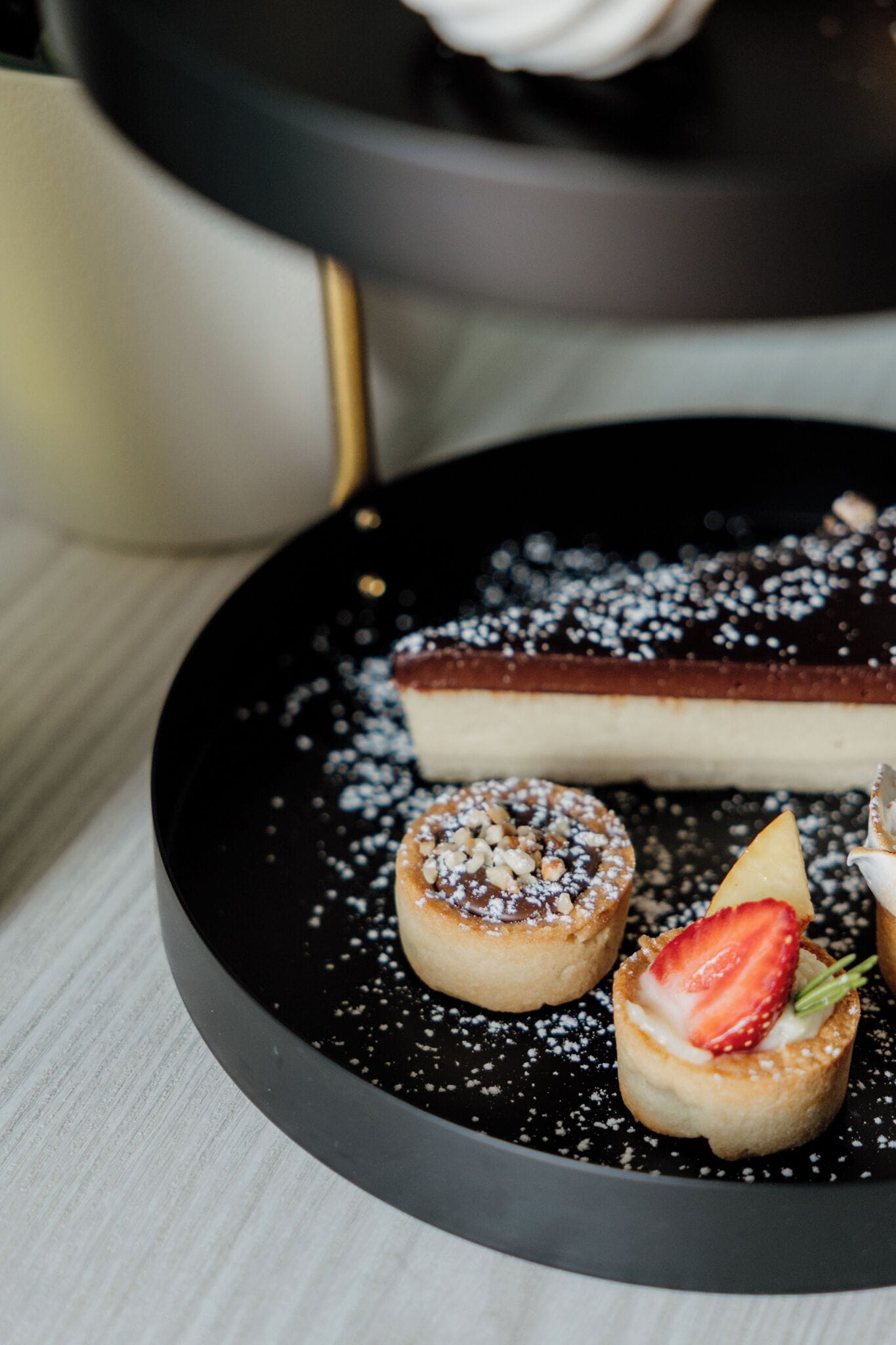A dessert plate with a cheesecake, two small tarts, and a strawberry on a black plate.
