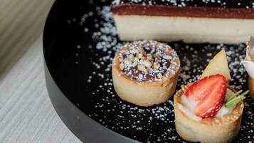 A dessert plate with a cheesecake, two small tarts, and a strawberry on a black plate.
