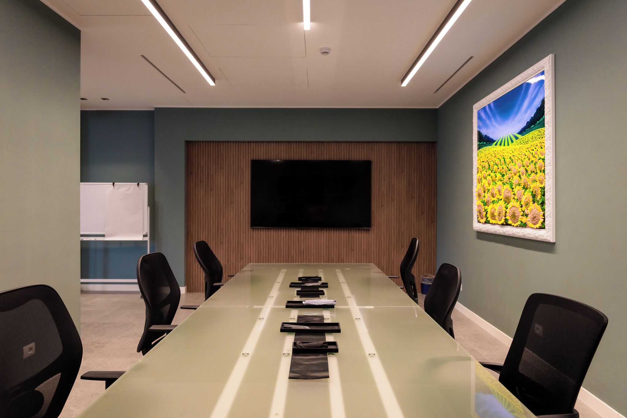 Una sala conferenze con un lungo tavolo, sedie, una TV a schermo piatto e un quadro appeso al muro.