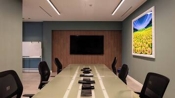Una sala conferenze con un lungo tavolo, sedie, una TV a schermo piatto e un quadro appeso al muro.
