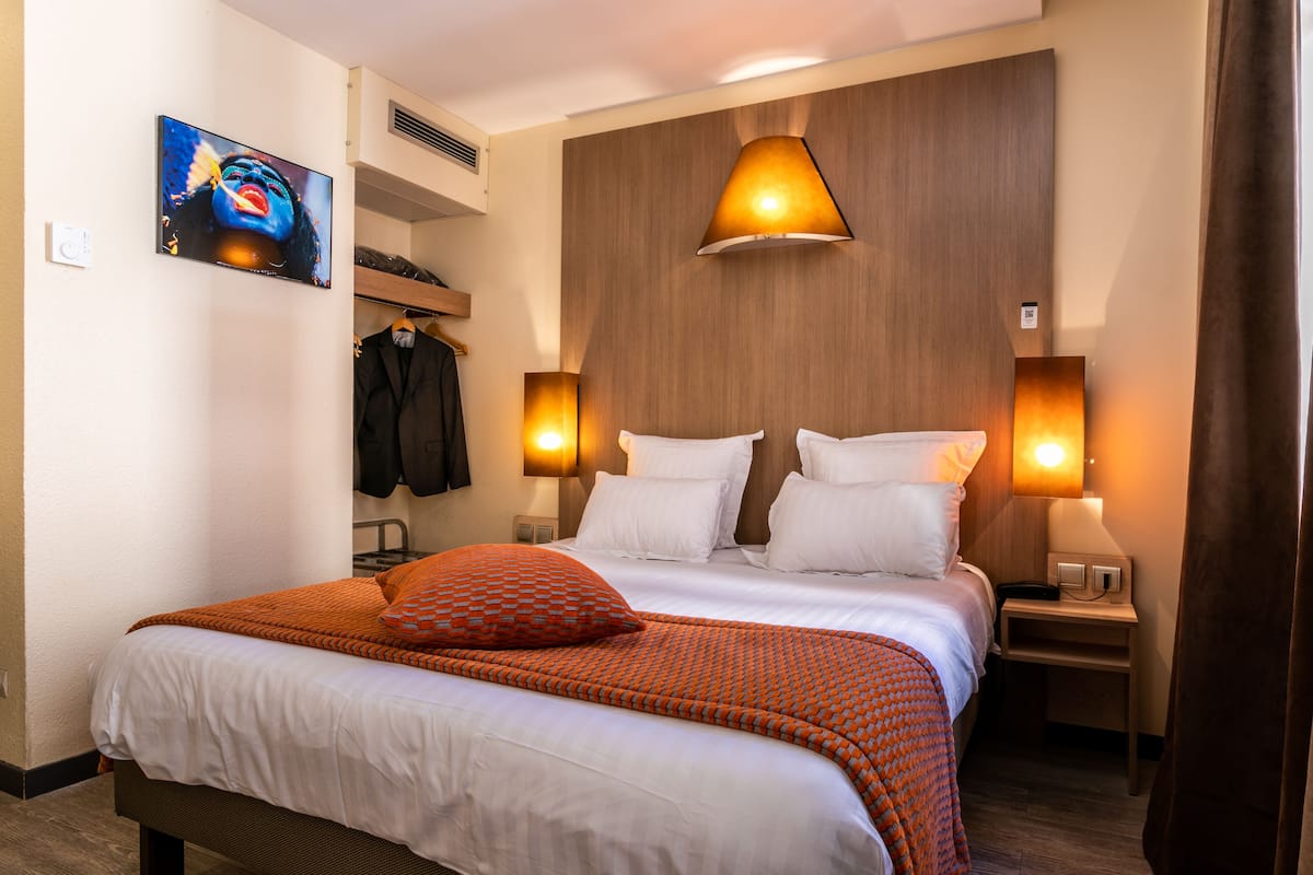 Ein Hotelzimmer mit einem großen Bett, zwei Nachttischen, einem an der Wand montierten Fernseher und einem Kleiderhaken.
