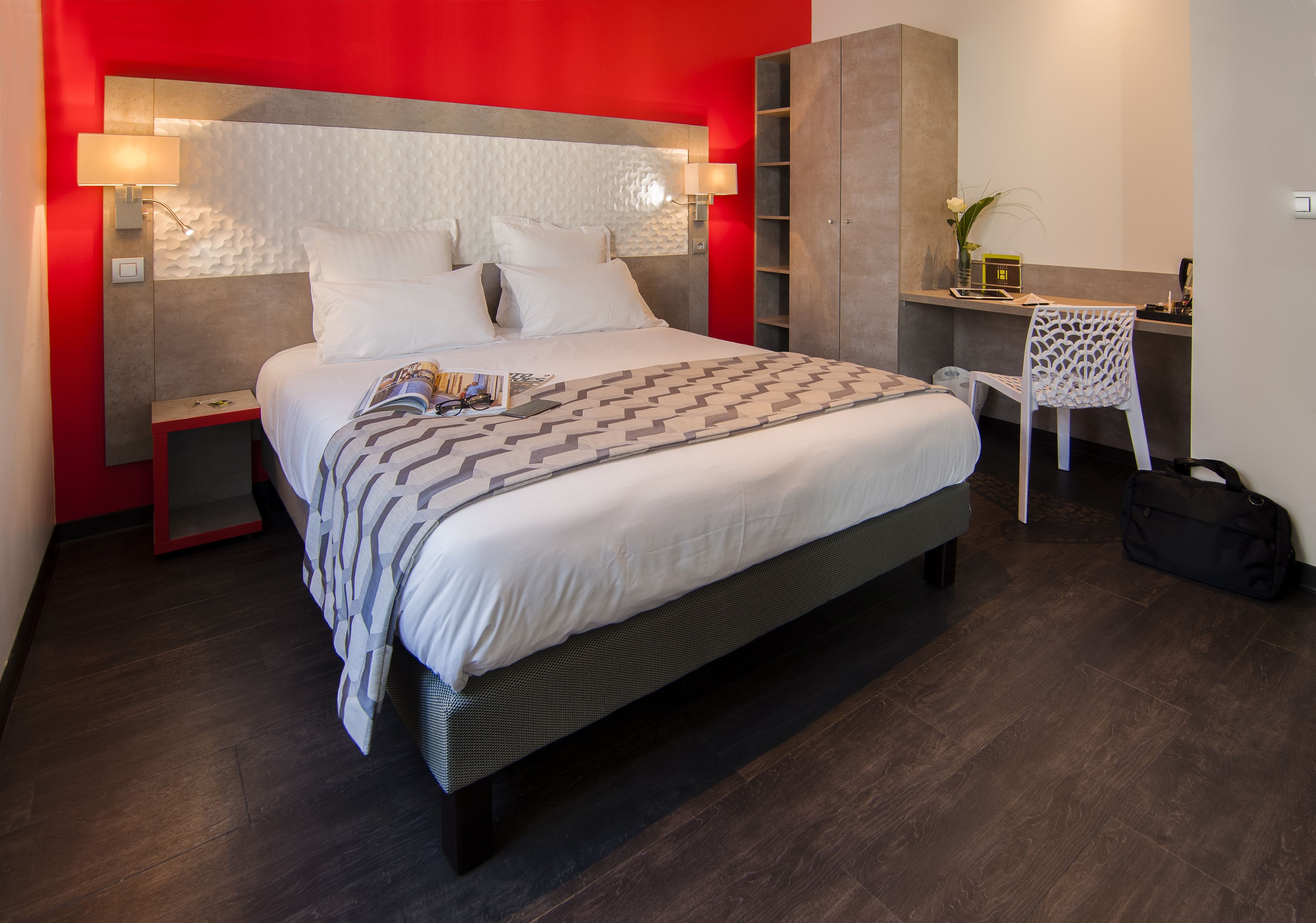 Quarto de hotel moderno com uma cama grande, mesa de cabeceira, escrivaninha com cadeira e guarda-roupa.