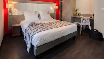 Quarto de hotel moderno com uma cama grande, mesa de cabeceira, escrivaninha com cadeira e guarda-roupa.