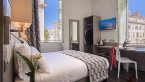 A hotel room with a bed, a desk, a chair, a TV, and a window with a city view.