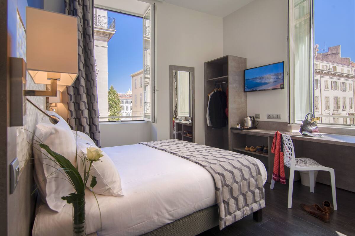 Ein Hotelzimmer mit Bett, Schreibtisch, Stuhl, Fernseher und Fenster mit Blick auf die Stadt.