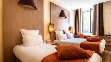 Habitación de hotel con dos camas, una ventana con cortinas y una lámpara de pared.
