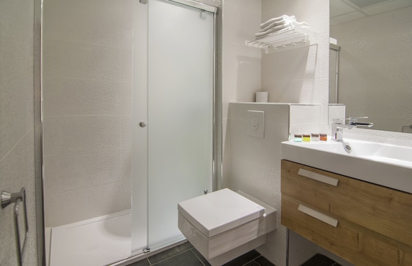 Un baño moderno con cabina de ducha de vidrio, un lavamanos blanco y un mueble de tocador de madera.