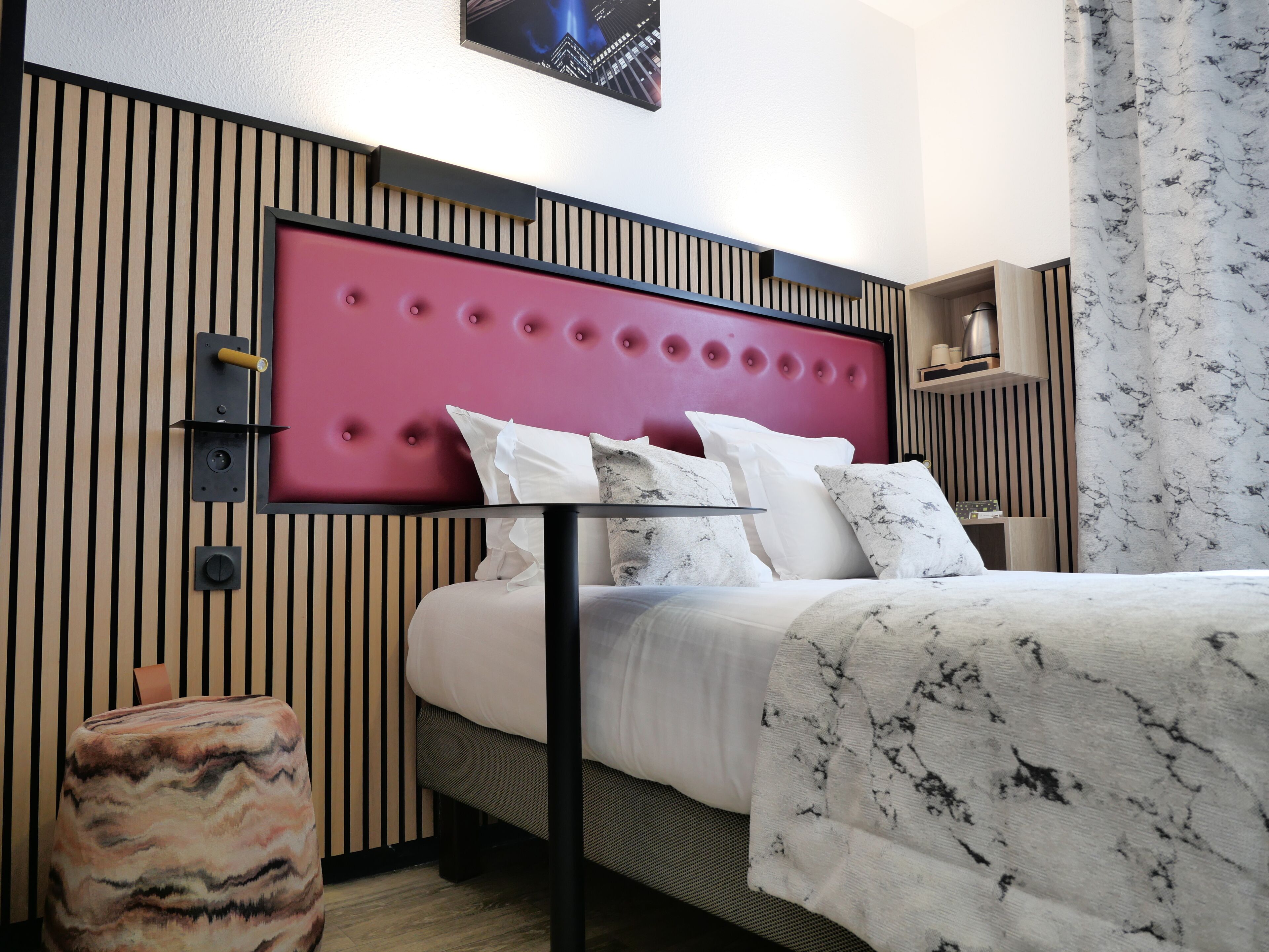Quarto de hotel moderno com cama, mesa de cabeceira e cabeceira com design acolchoado.