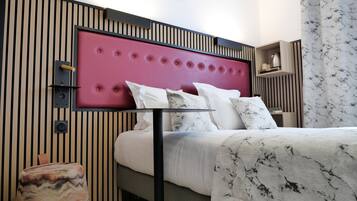 Quarto de hotel moderno com cama, mesa de cabeceira e cabeceira com design acolchoado.