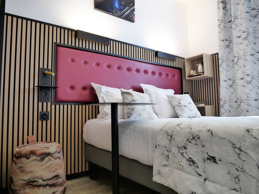 Quarto de hotel moderno com cama, mesa de cabeceira e cabeceira com design acolchoado.