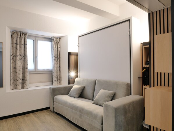 A modern living room with a sofa, a window with curtains, and a built-in TV. - Hôtel Carré Vieux Port (Marseille)
