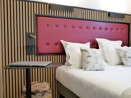 A neatly arranged hotel room with a bed, pillows, a small table, and a chair.