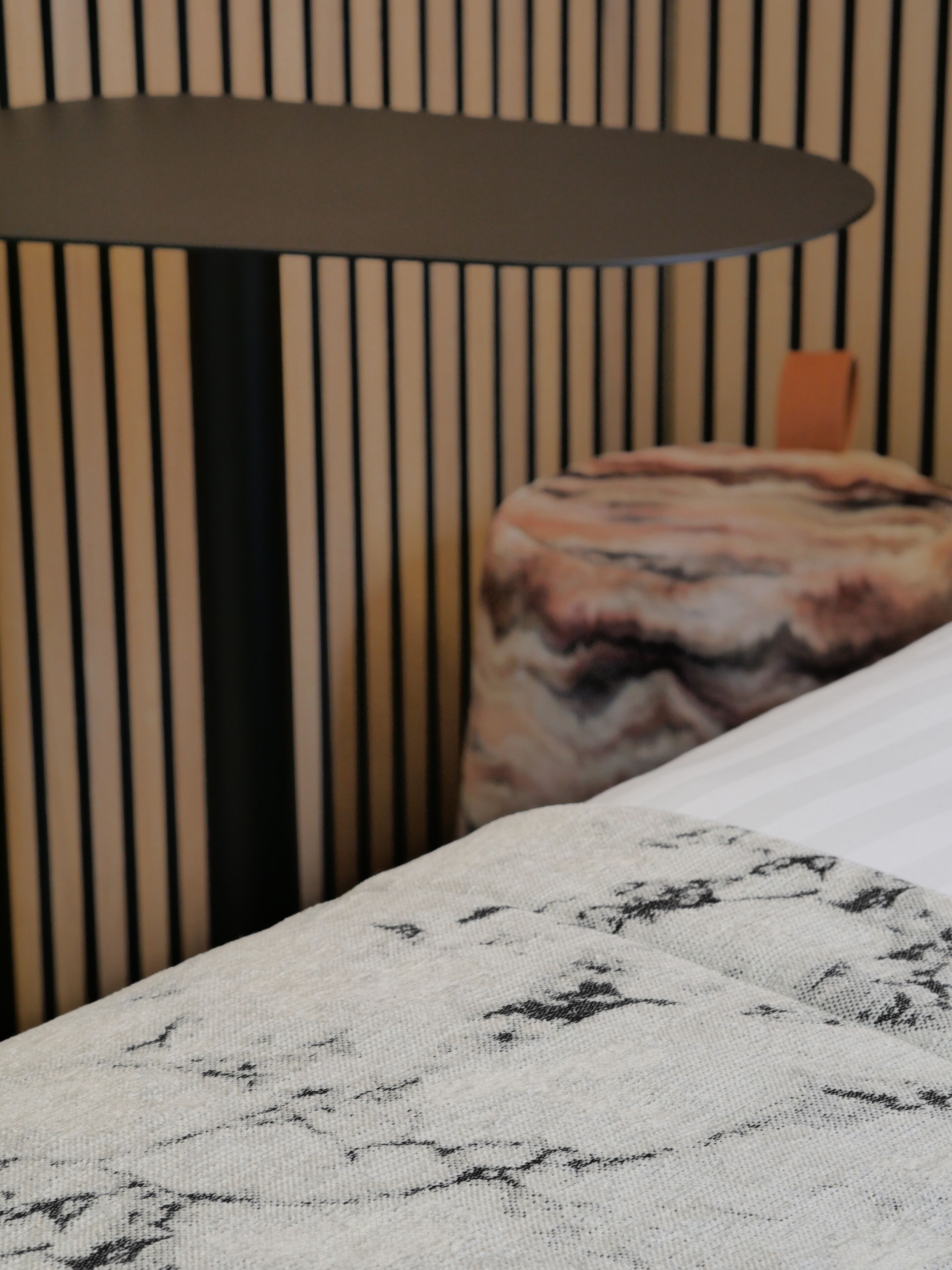 Una cama con colcha estampada, un almohadón con diseño marmolado y cabecera con listones verticales.