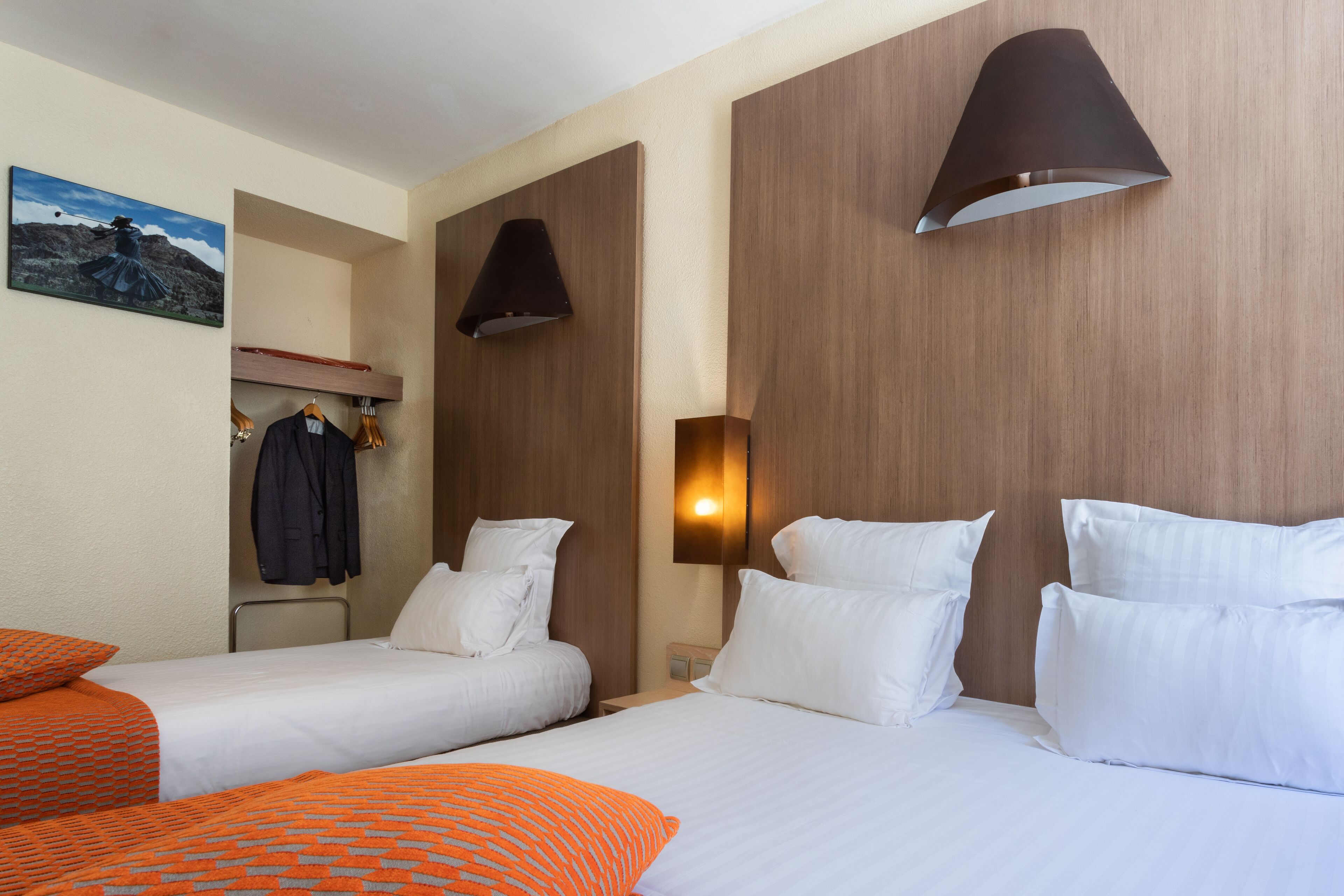 A hotel room with two beds, a wardrobe, and a painting on the wall.