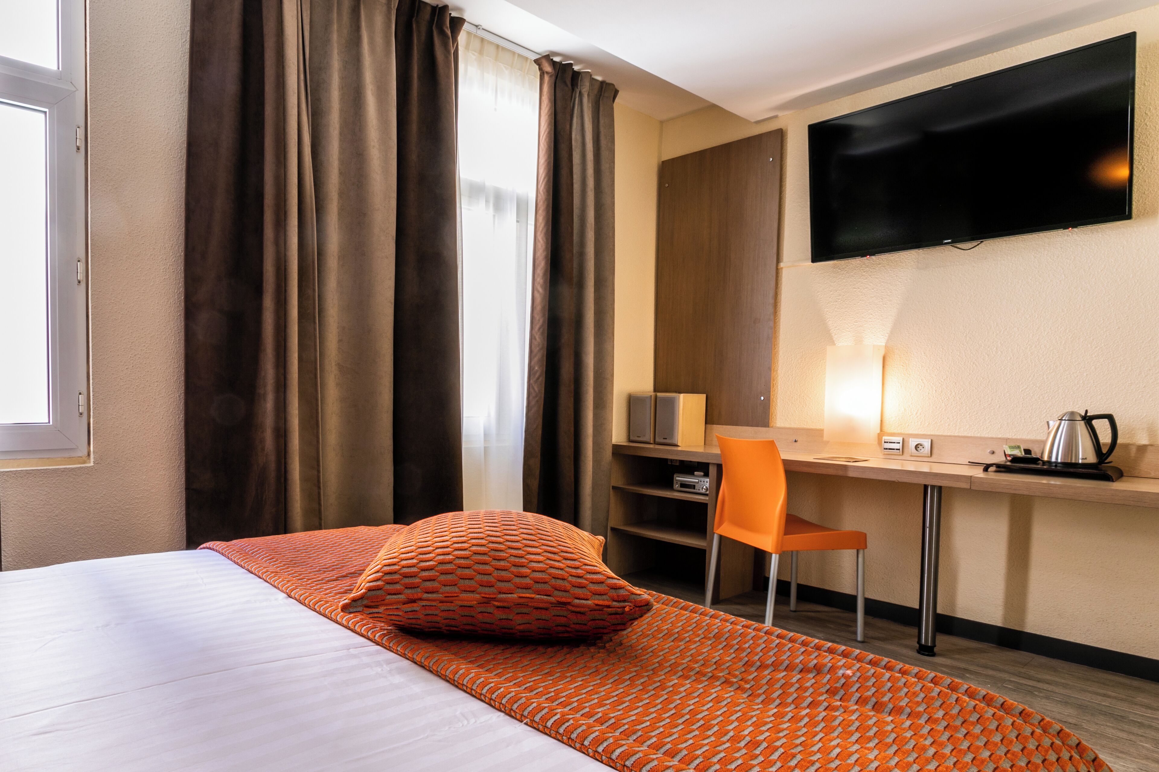 A hotel room with a bed, a desk, a chair, a television, and a coffee maker.