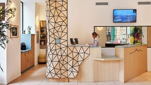 A reception area with a geometric wooden ceiling design, a reception desk, a television mounted on the wall, and a view of the cityscape through the window.