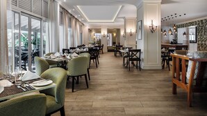 Un comedor amplio con varias mesas y sillas, ventanas grandes y una lámpara moderna.