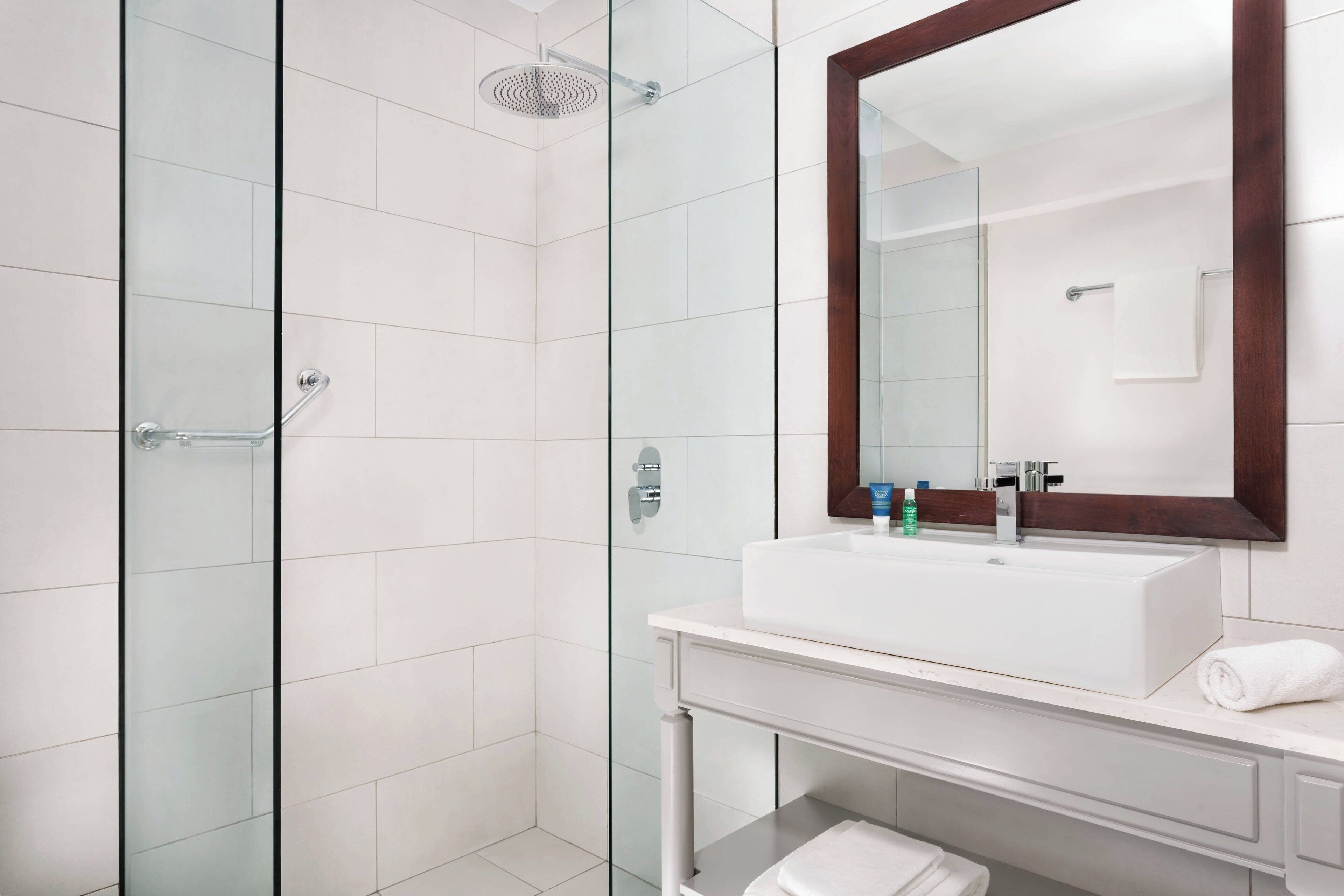 A modern bathroom with a glass shower enclosure, a white sink, and a large mirror with a wooden frame.