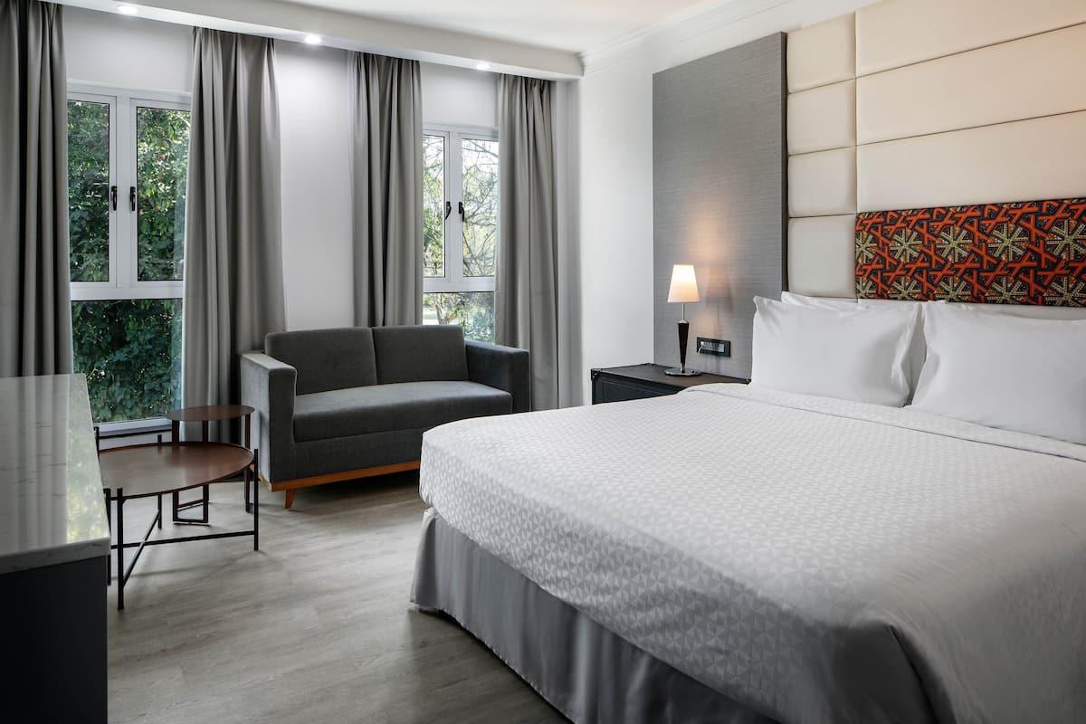 Ein modernes Hotelzimmer mit einem großen Bett, einer Couch, einem kleinen Tisch und einem Fenster mit Vorhängen.