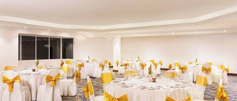 A banquet hall with round tables set for dining, each with white tablecloths and gold sashes.
