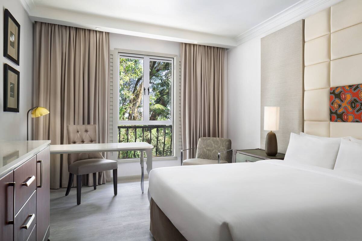 Ein Hotelzimmer mit Bett, Schreibtisch, Stuhl und einem Balkon mit Vorhängen.