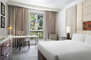 Habitación de hotel con cama, escritorio, silla y balcón con cortinas.