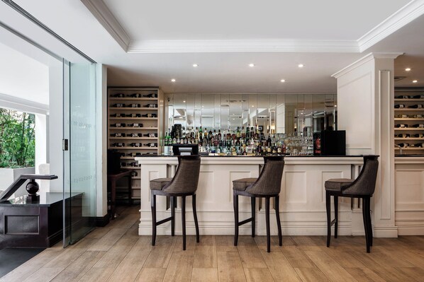 A bar area with three bar stools, a wine rack, and a mirrored wall.