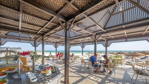 An outdoor dining area with a covered patio, tables, chairs, and a buffet with various food items. - Marhaba Beach (Sousse)