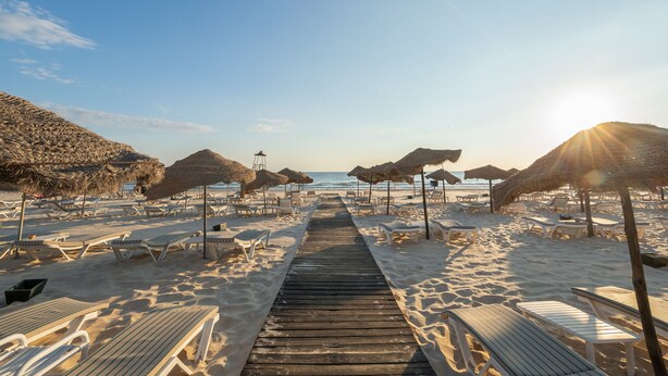 A beach with a wooden walkway leading to the sea, surrounded by sun loungers and thatched umbrellas. - Marhaba Beach (Sousse)