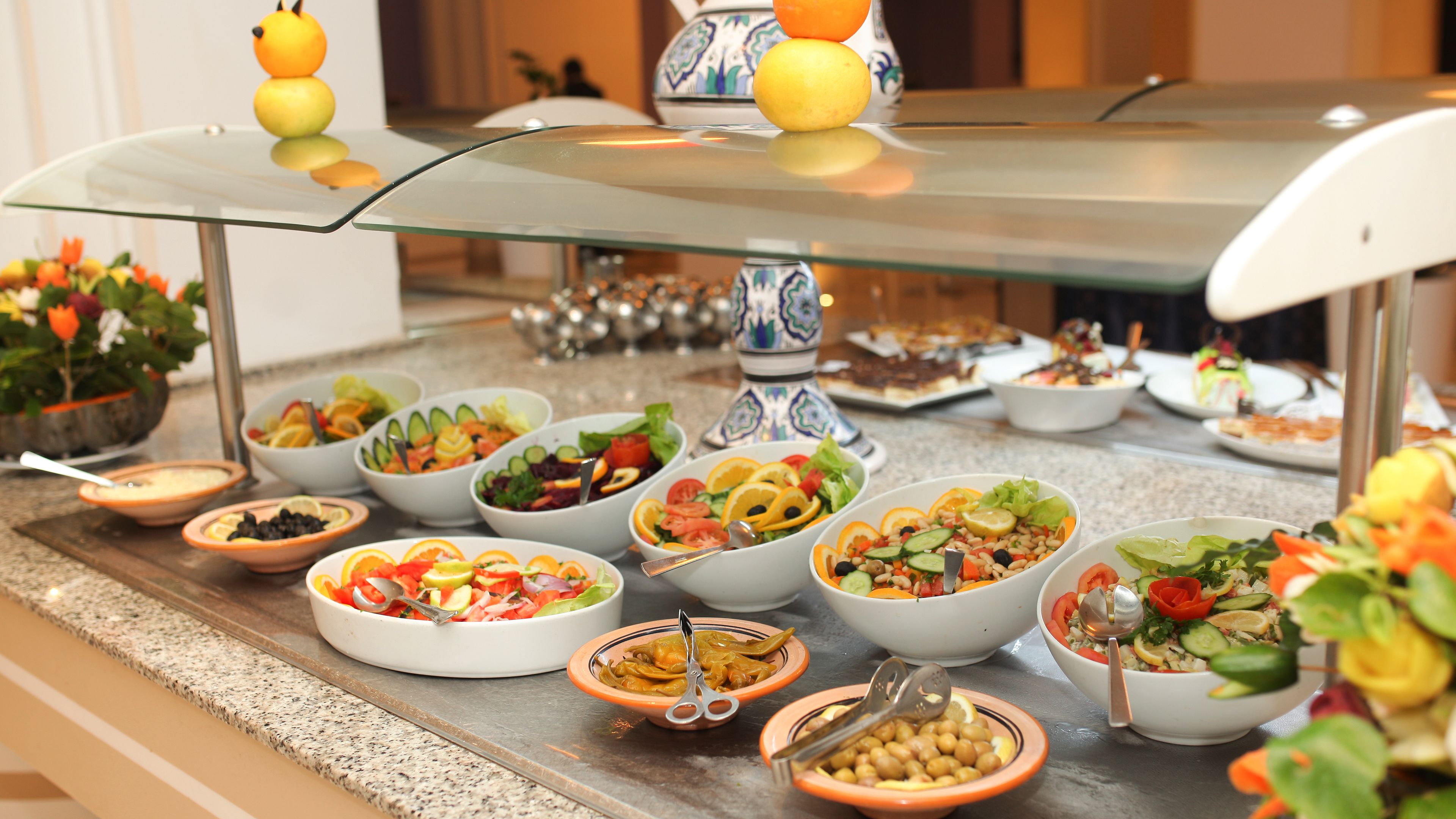A buffet with various dishes, including salads and bowls of food, arranged on a glass-top table.