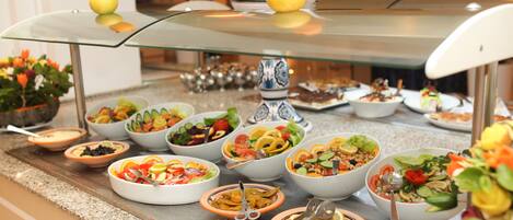 A buffet with various dishes, including salads and bowls of food, arranged on a glass-top table.
