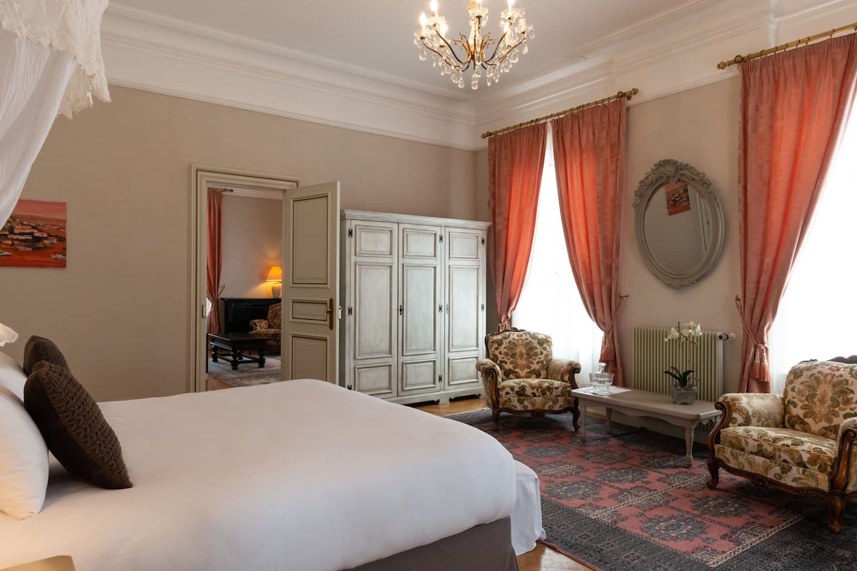 Un dormitorio con una cama grande, una zona de estar con dos sillones, una mesa y un armario.