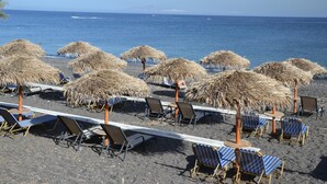 A beach with rows of sun loungers and thatched umbrellas, a clear sky, and the ocean in the background.