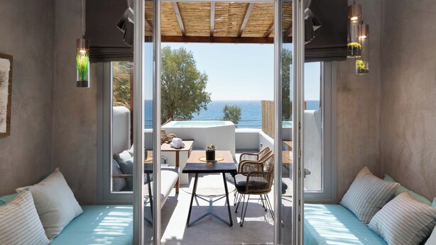 A modern room with a glass wall, a wooden ceiling, and a view of the sea.
