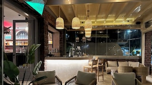 A bar area with wicker furniture and hanging lights, a bar counter, and a view of the night outside.