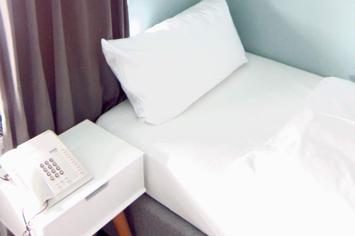 A hotel room with a bed, a bedside table with a phone, and a wall-mounted light fixture.