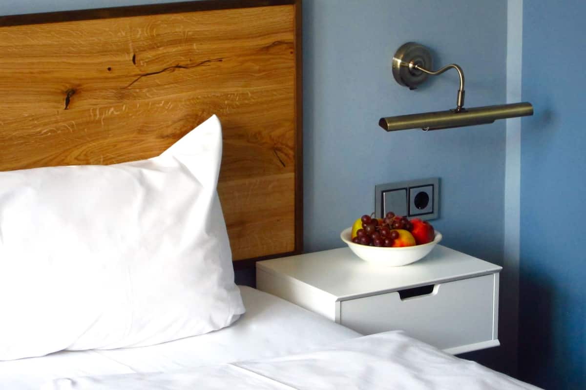 A neatly made bed with a wooden headboard, a white pillow, and a bedside table with a bowl of fruit.