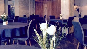 A restaurant with round tables and black chairs, featuring a vase of white flowers in the foreground. - Hotel Zentrum (Frankfurt)