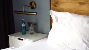 A neatly made bed with white linens, a wooden headboard, a bedside table with a bottle and glass, and a wall-mounted light fixture. - Hotel Zentrum (Frankfurt)