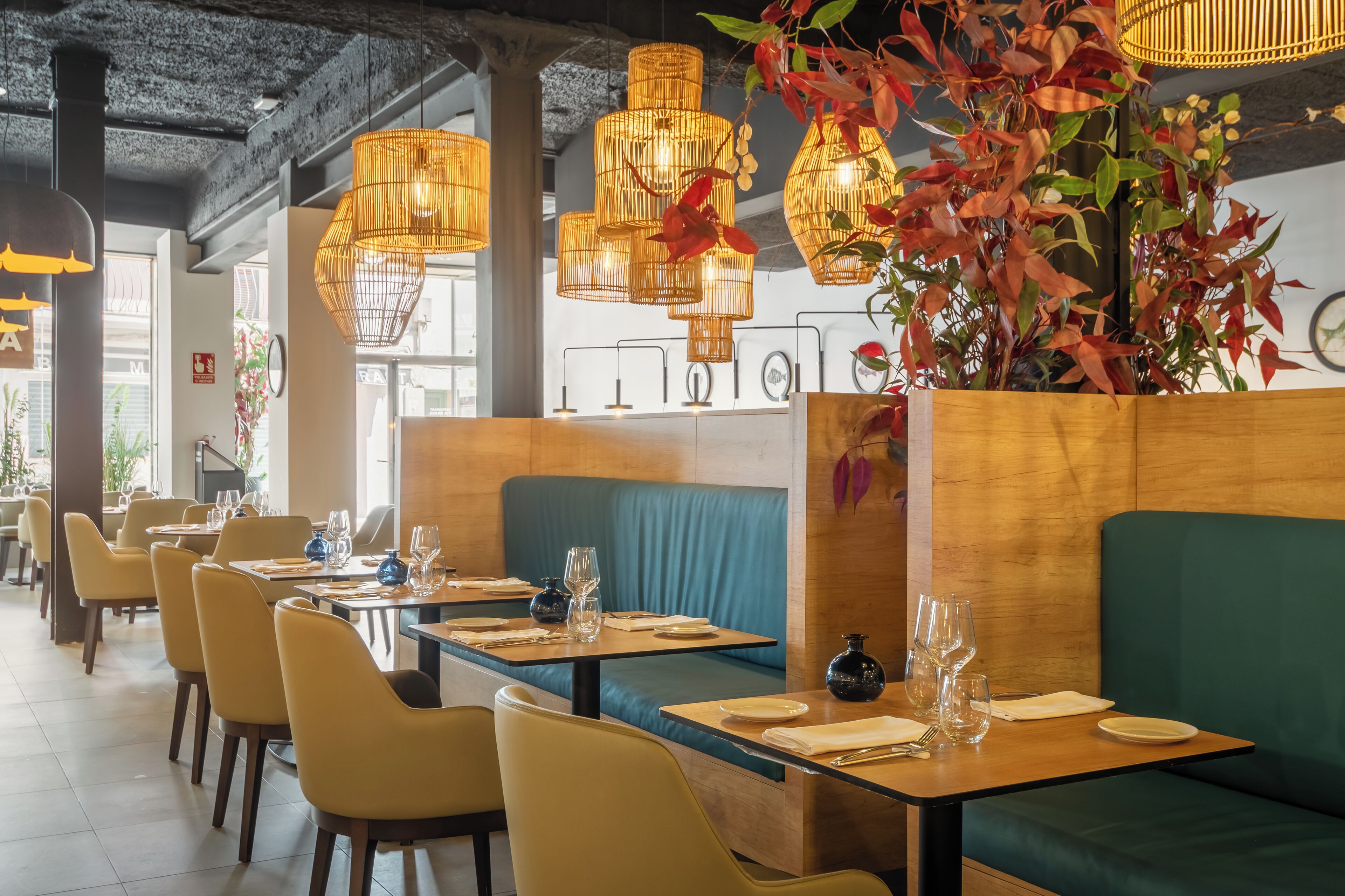 L’intérieur d’un restaurant avec des tables en bois, des banquettes vertes rembourrées et des lampes en osier suspendues au plafond.