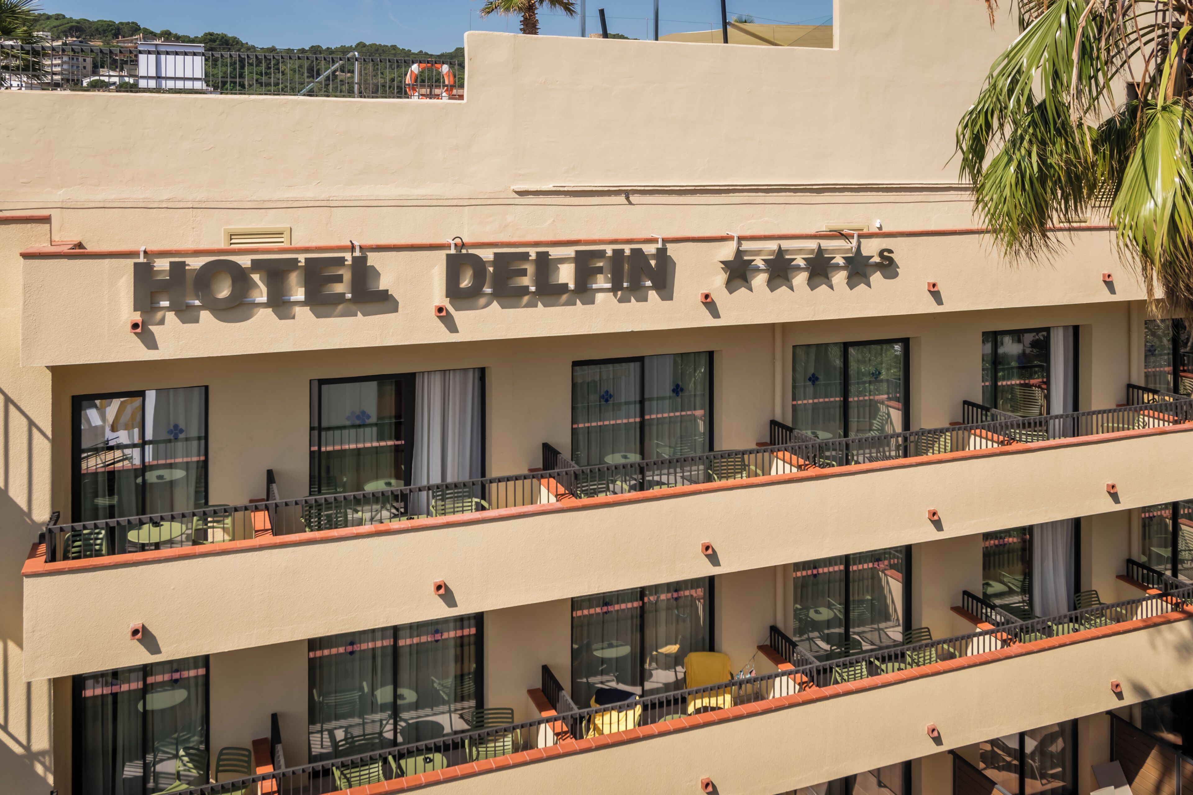 A hotel with a sign reading 'HOTEL DELFIN' and balconies with outdoor seating.