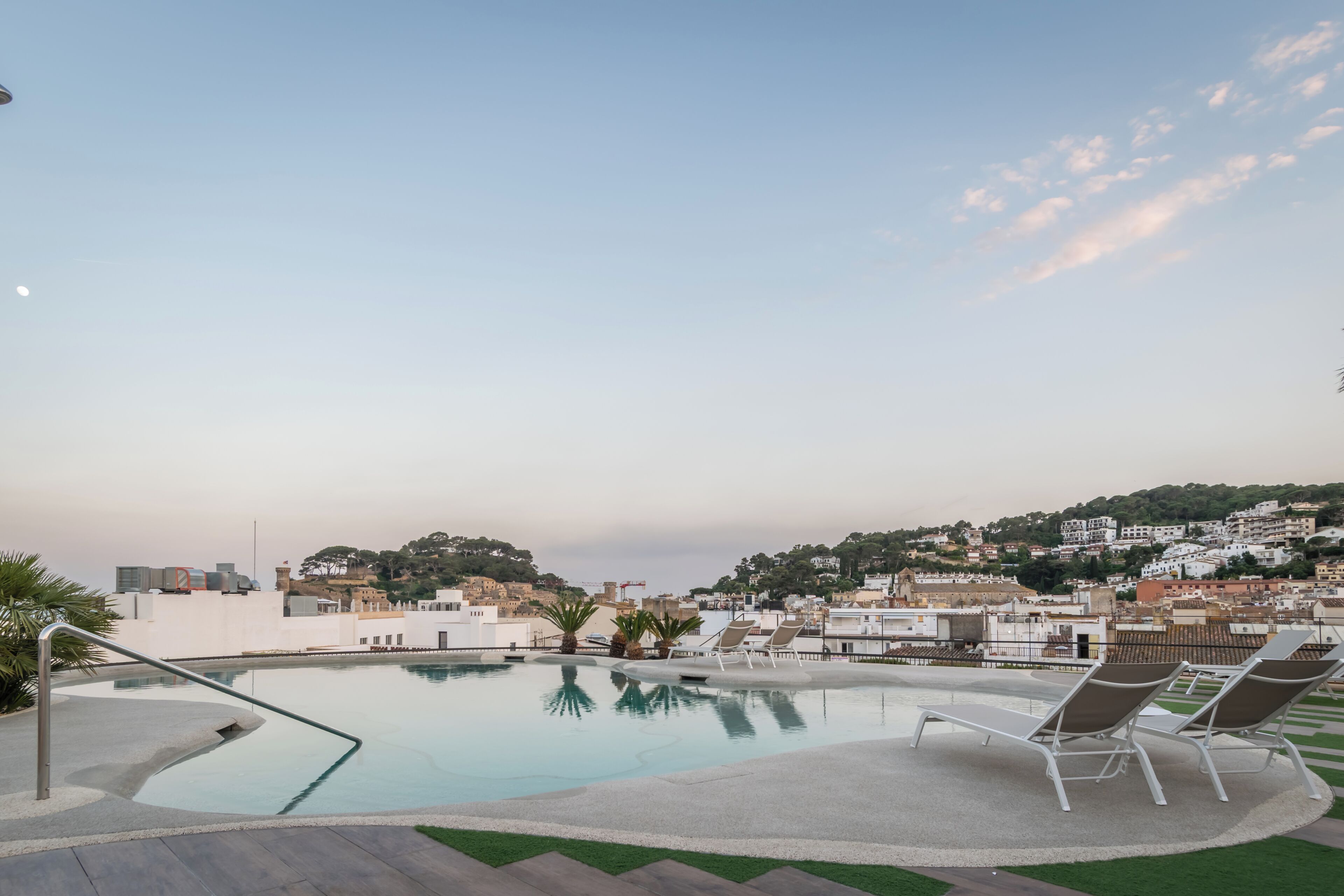 Una piscina en la azotea con sillones, vistas despejadas del paisaje urbano y una colina distante.