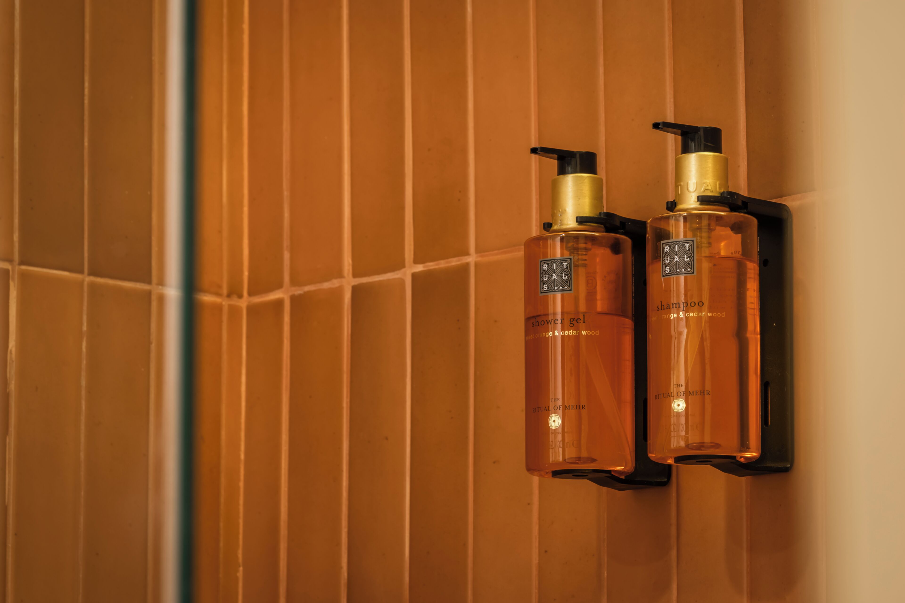 Two bottles of Rituals shower gel and shampoo mounted on a wall.