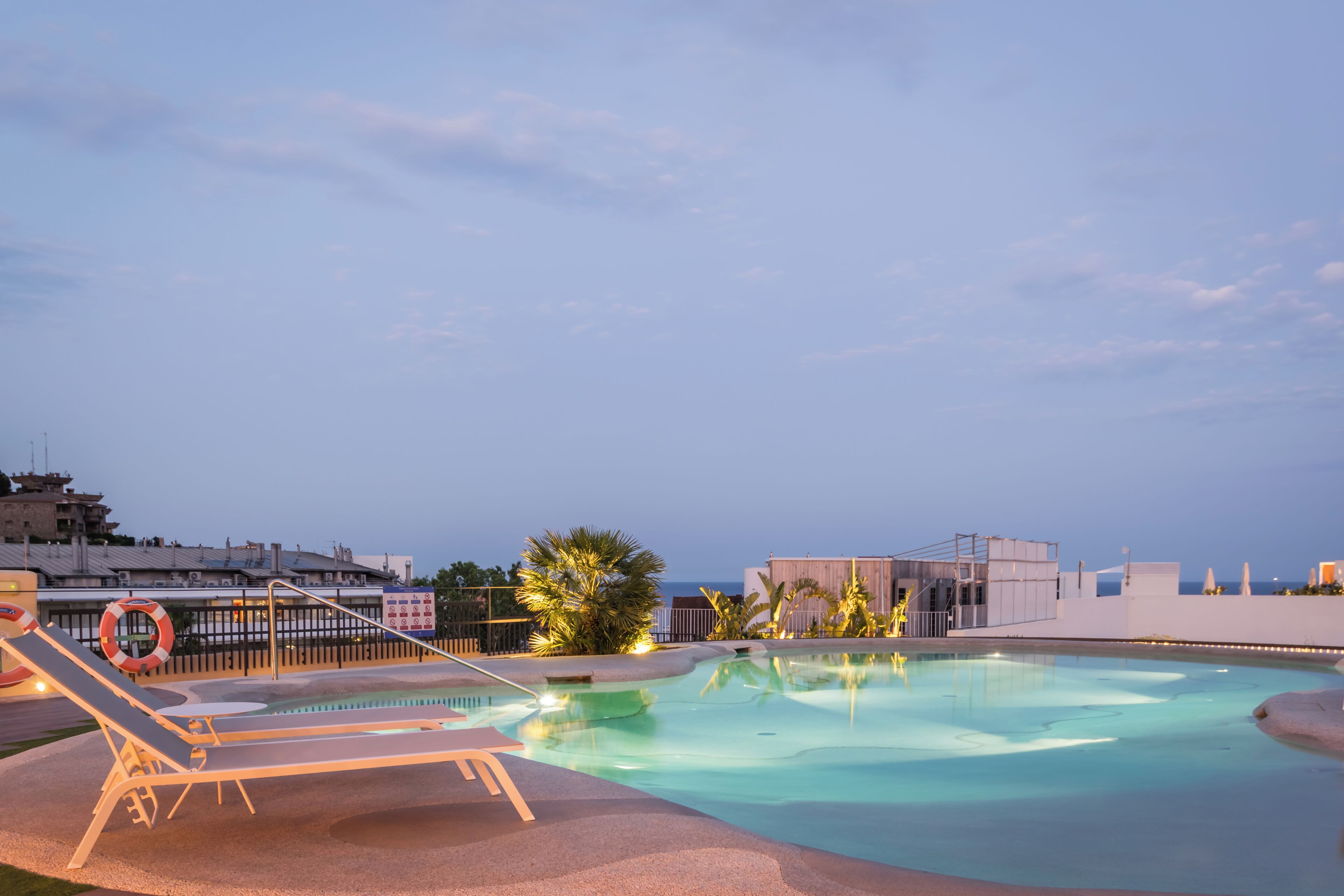 Una piscina con sillas de descanso y un flotador, rodeada de palmeras y edificios.